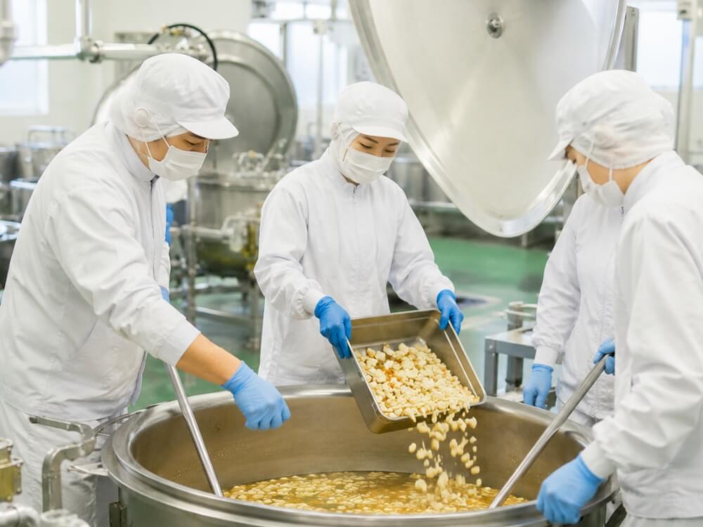 調理された食材を大鍋から移す食品工場の従業員